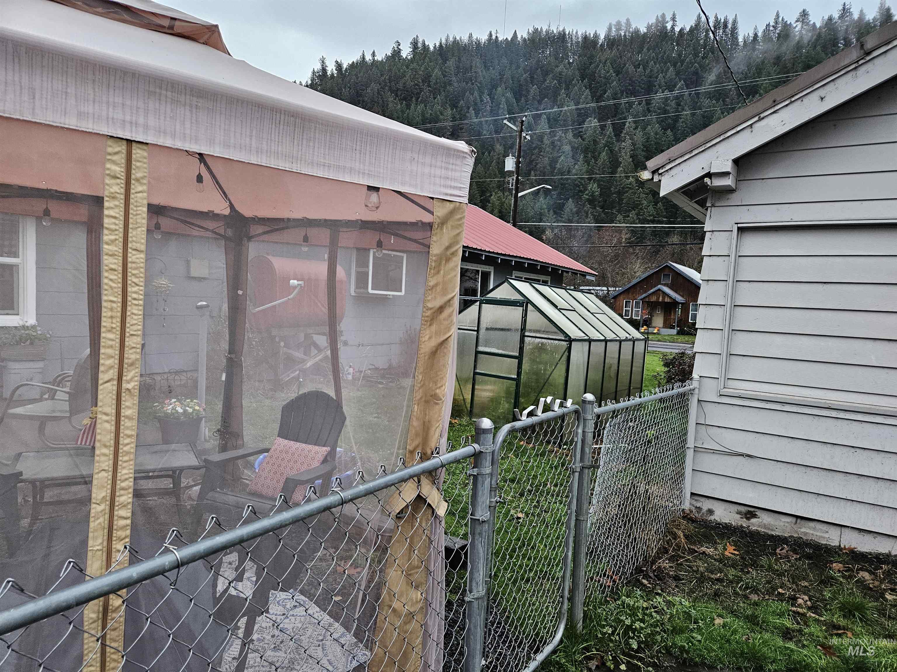 View of side of property featuring a greenhouse, an outbuilding, a wooded view, a sunroom, and a gate