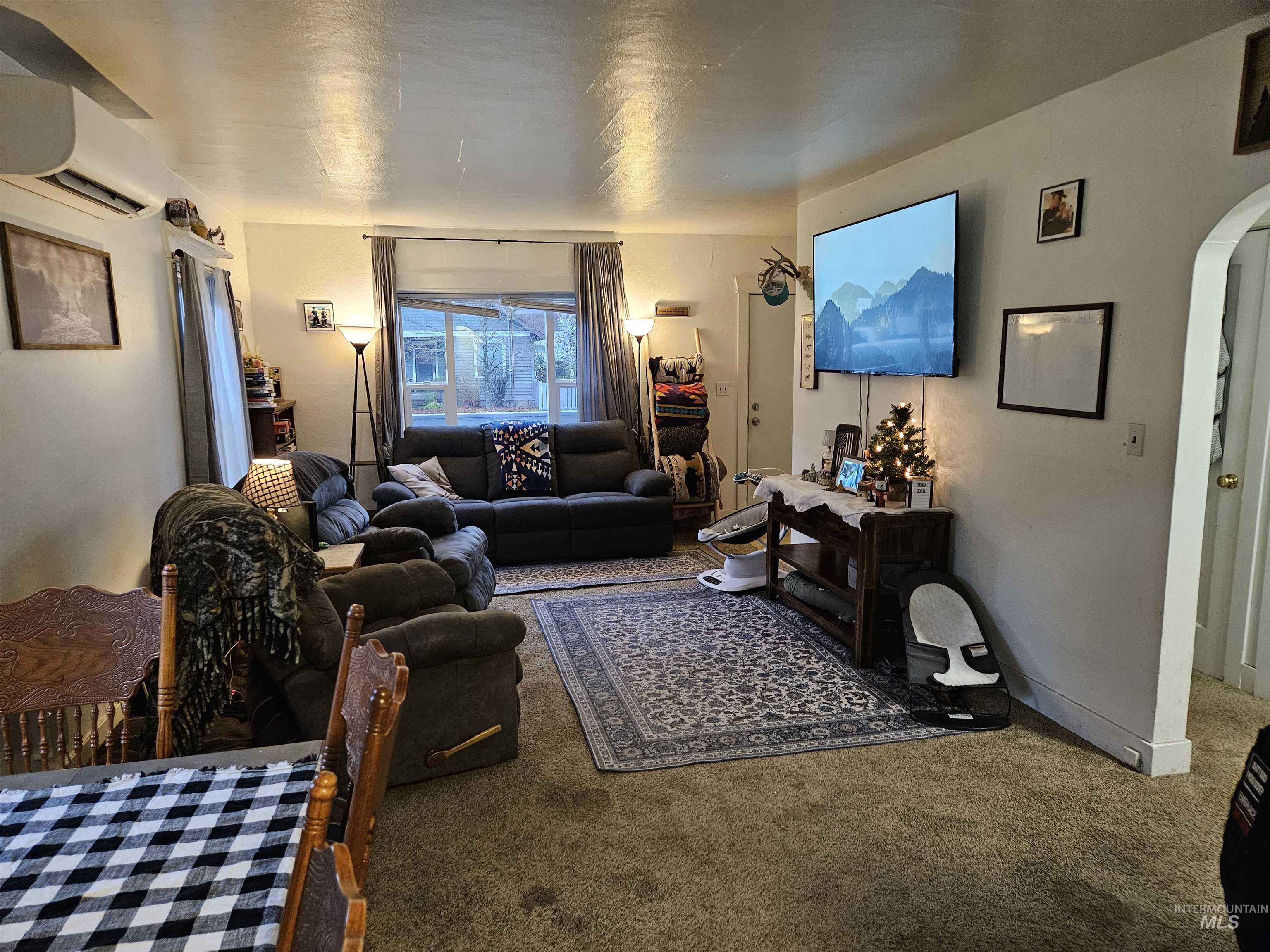 Carpeted living room with arched walkways and a wall mounted air conditioner