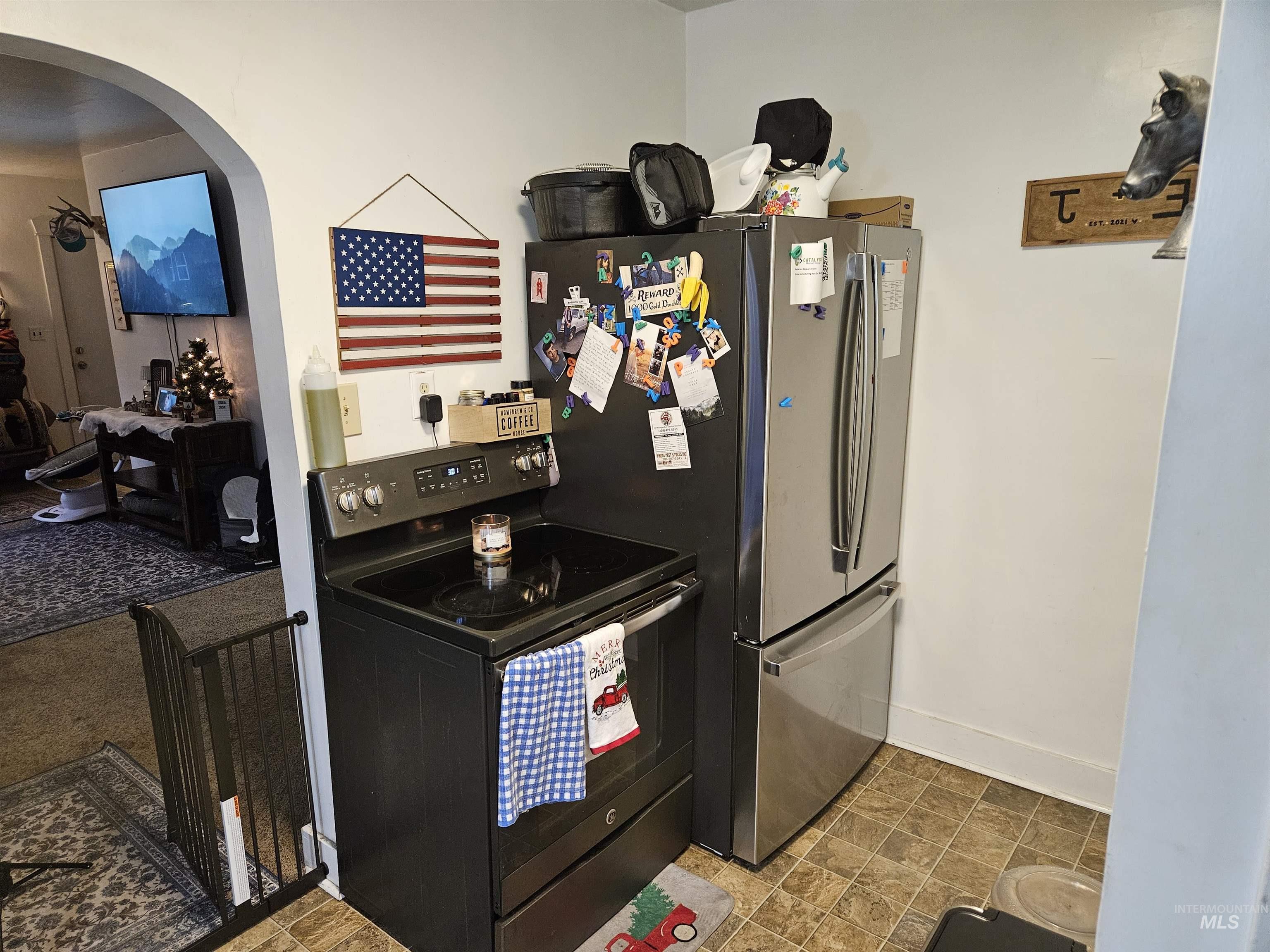Kitchen with black range with electric stovetop, arched walkways, and freestanding refrigerator