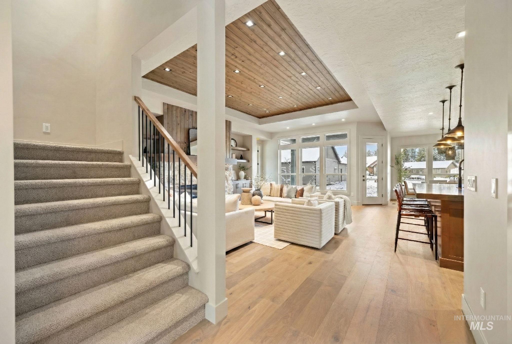 Living room featuring a raised ceiling, stairs, light wood-style floors, and recessed lighting