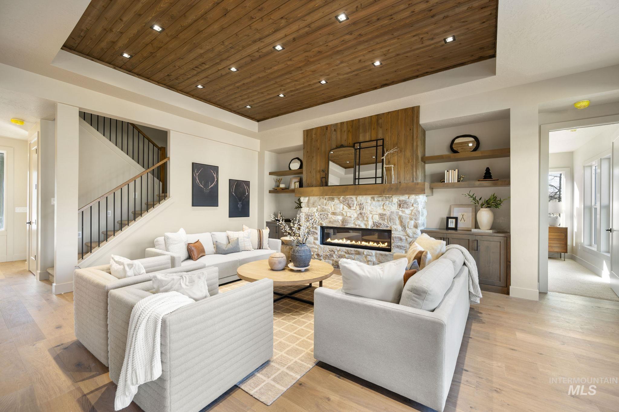 Living room featuring a tray ceiling, built in shelves, wooden ceiling, a stone fireplace, and stairway