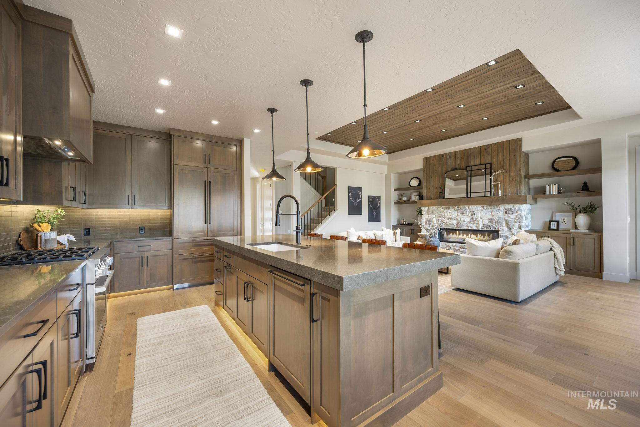 Kitchen with decorative light fixtures, a raised ceiling, open floor plan, a stone fireplace, and high end stove