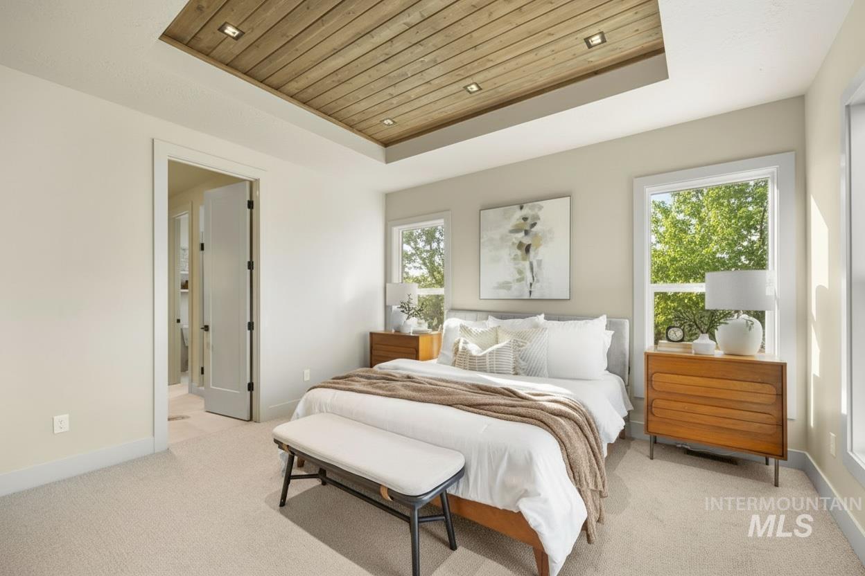 Bedroom featuring a tray ceiling, wooden ceiling, light colored carpet, recessed lighting, and connected bathroom