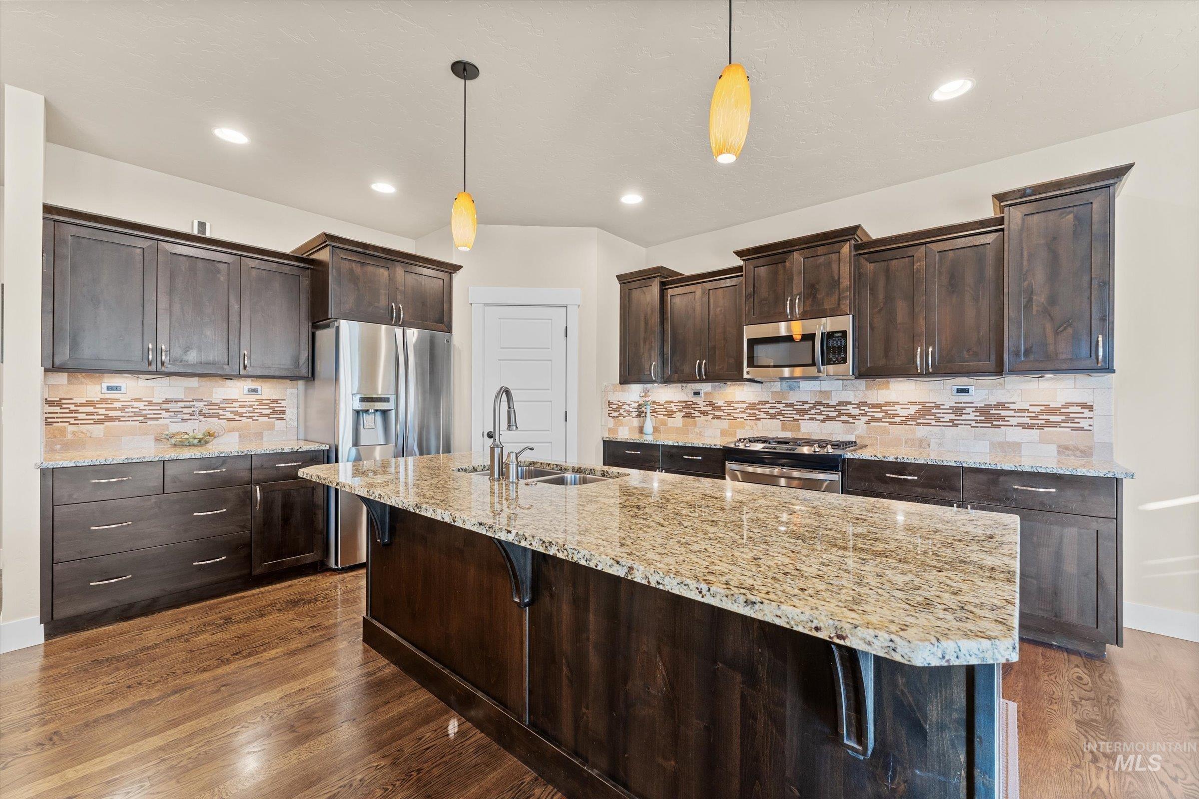 Kitchen with dark brown cabinetry, backsplash, hanging light fixtures, light stone counters, and recessed lighting