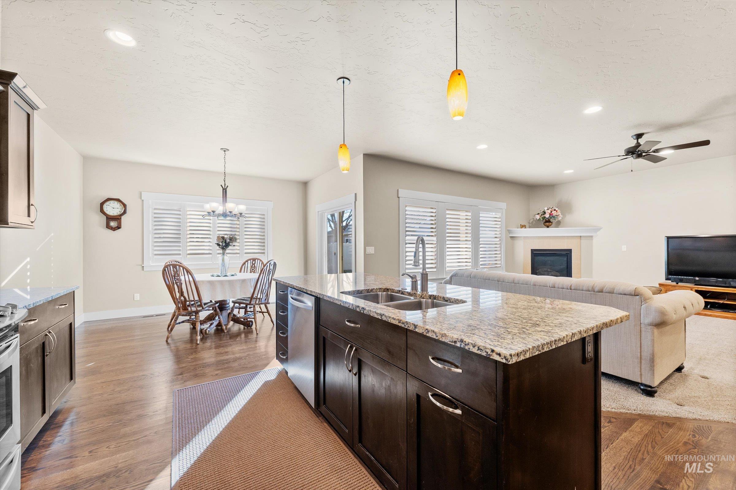 Kitchen featuring dark brown cabinetry, pendant lighting, light stone counters, a tile fireplace, and recessed lighting
