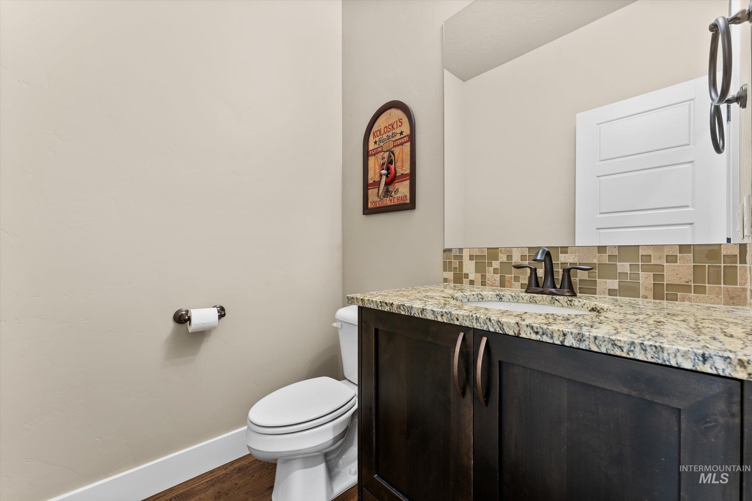 Half bath featuring tasteful backsplash, vanity, and dark wood-style flooring