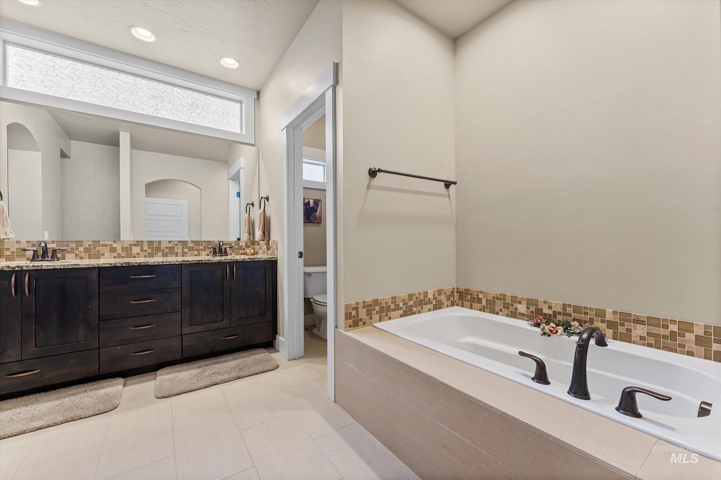 Bathroom with double vanity, backsplash, a bath, light tile patterned floors, and recessed lighting