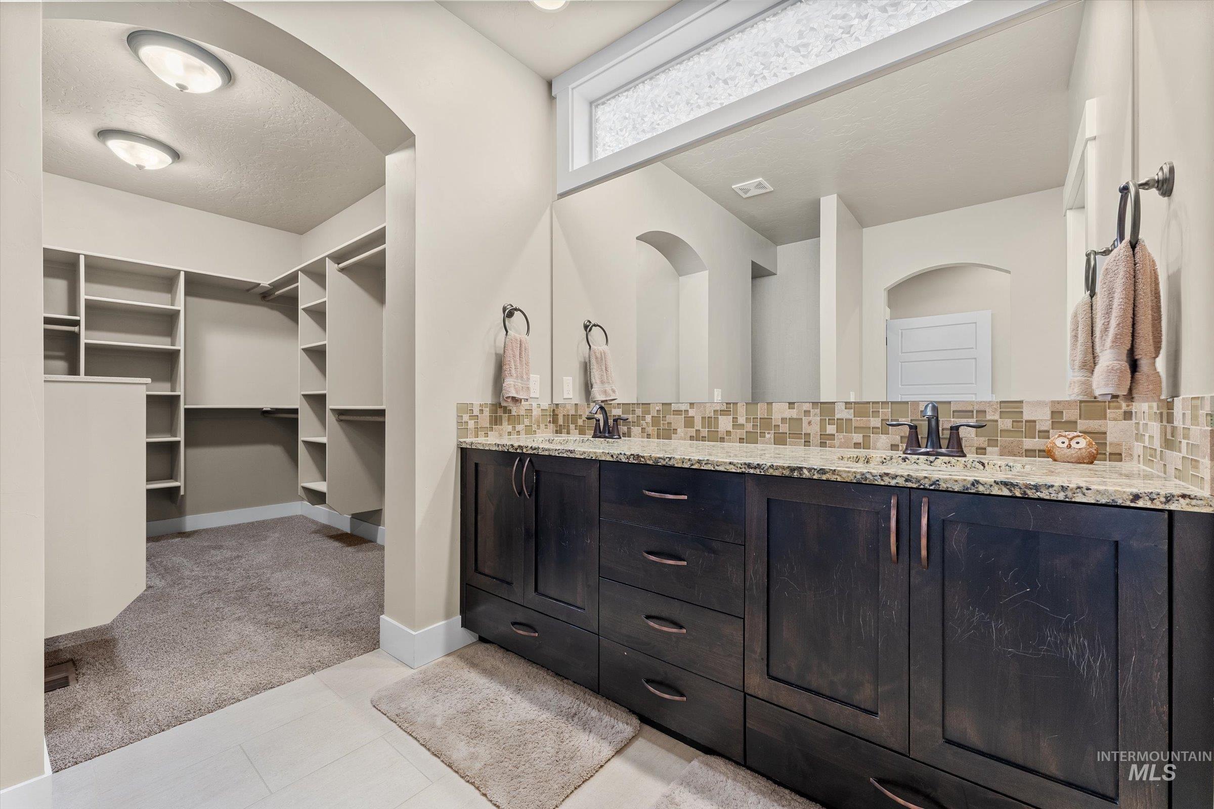 Full bathroom featuring double vanity, a walk in closet, light carpet, backsplash, and a textured ceiling