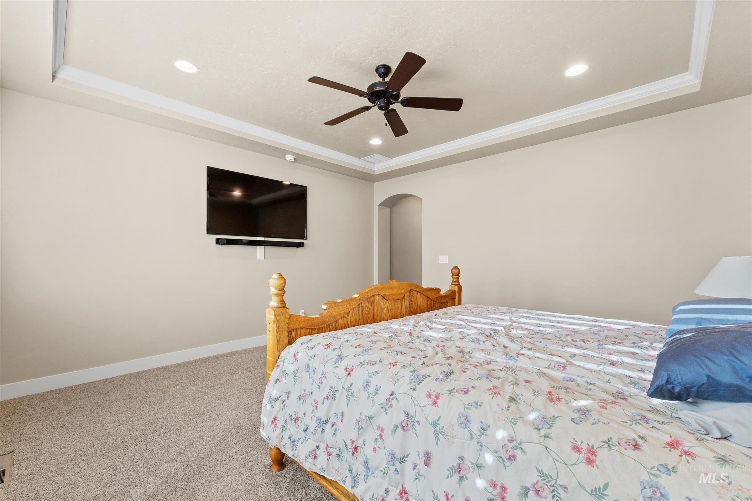 Carpeted bedroom featuring a tray ceiling, arched walkways, a ceiling fan, and recessed lighting