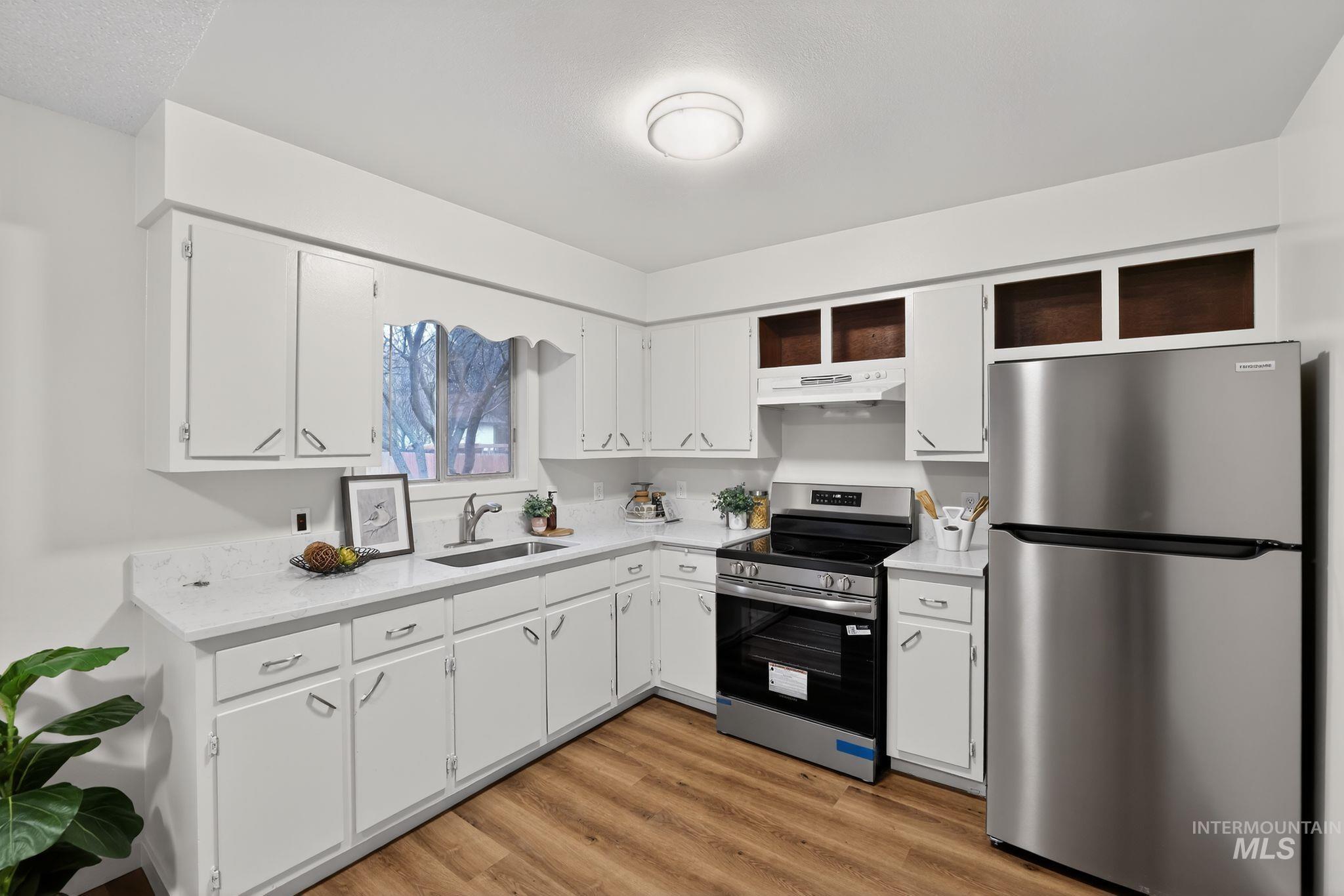 Kitchen featuring stainless steel appliances, white cabinetry, light wood-style flooring, and light stone countertops