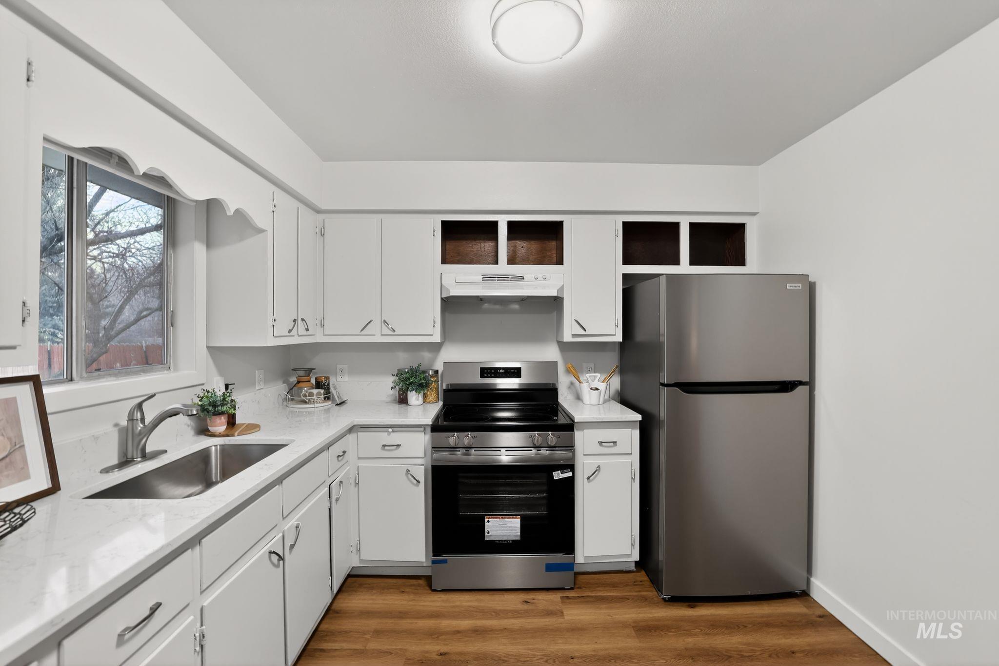 Kitchen with appliances with stainless steel finishes, white cabinetry, dark wood-style floors, and light stone countertops
