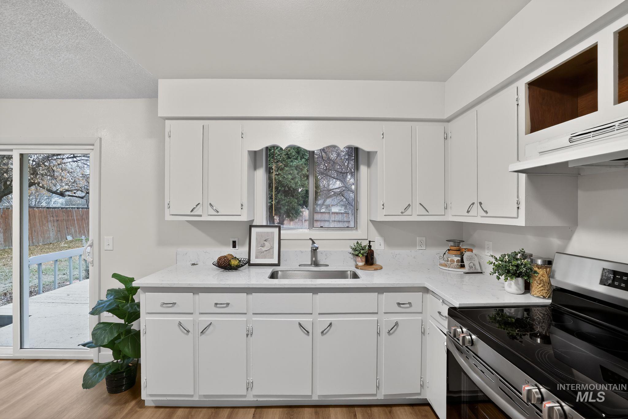 Kitchen with stainless steel electric range, white cabinets, light stone counters, and light wood-style flooring