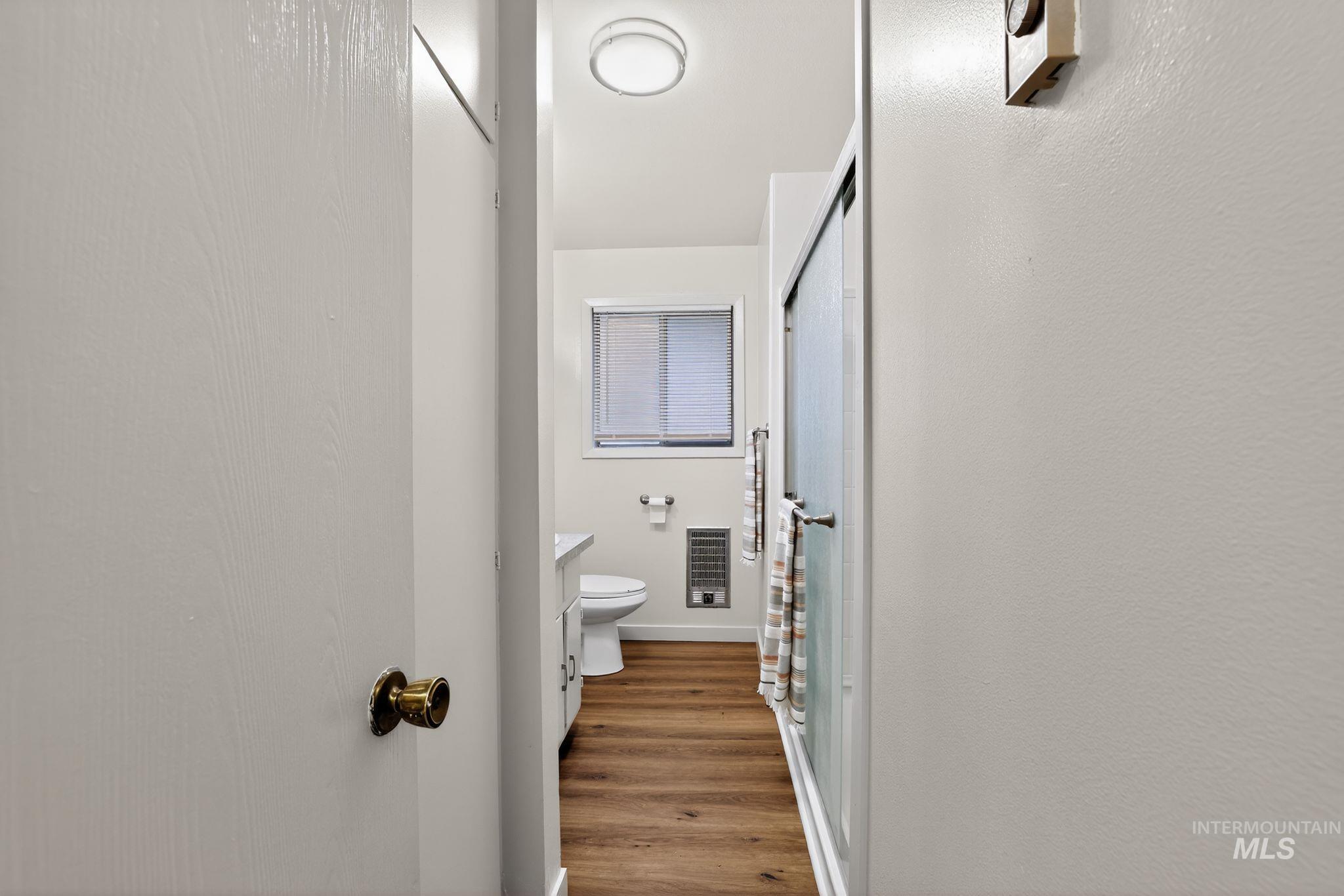 Bathroom featuring vanity, a stall shower, wood finished floors, and heating unit
