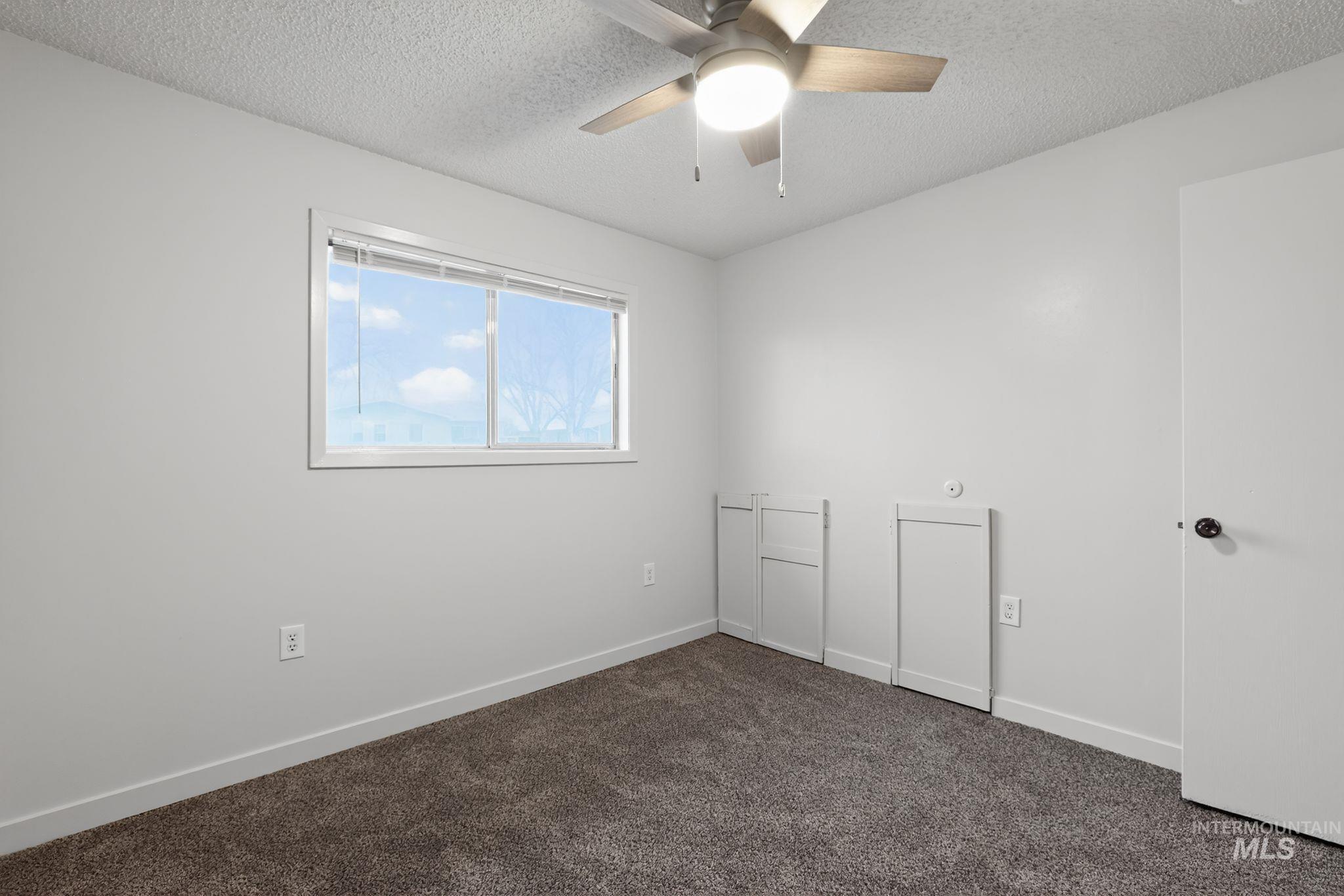Empty room with a textured ceiling, dark colored carpet, and a ceiling fan