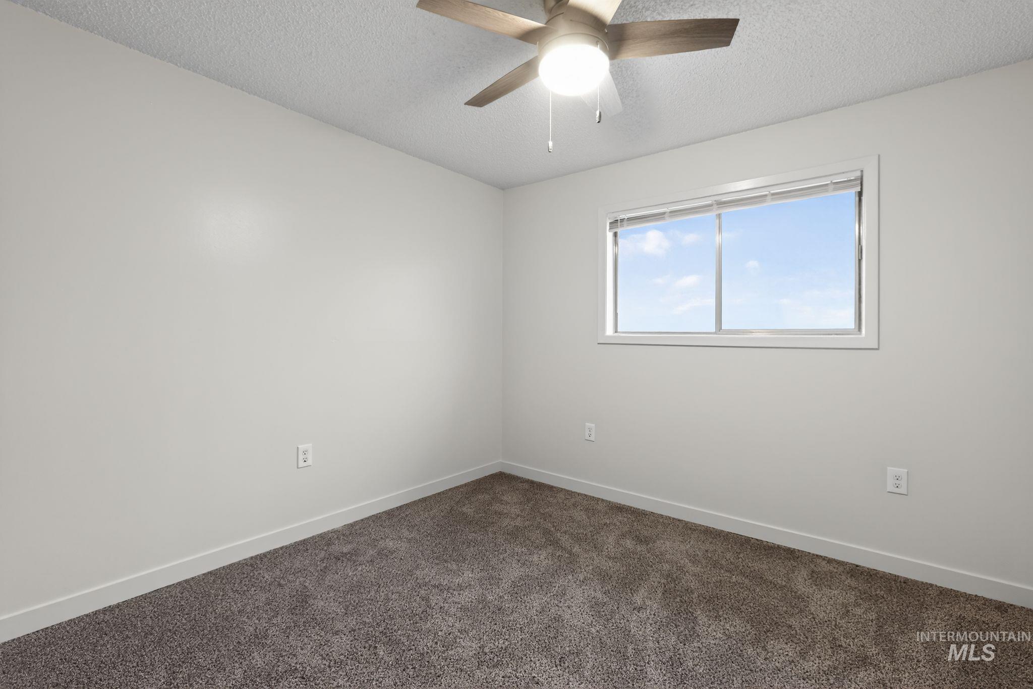 Spare room with a textured ceiling, dark colored carpet, and ceiling fan