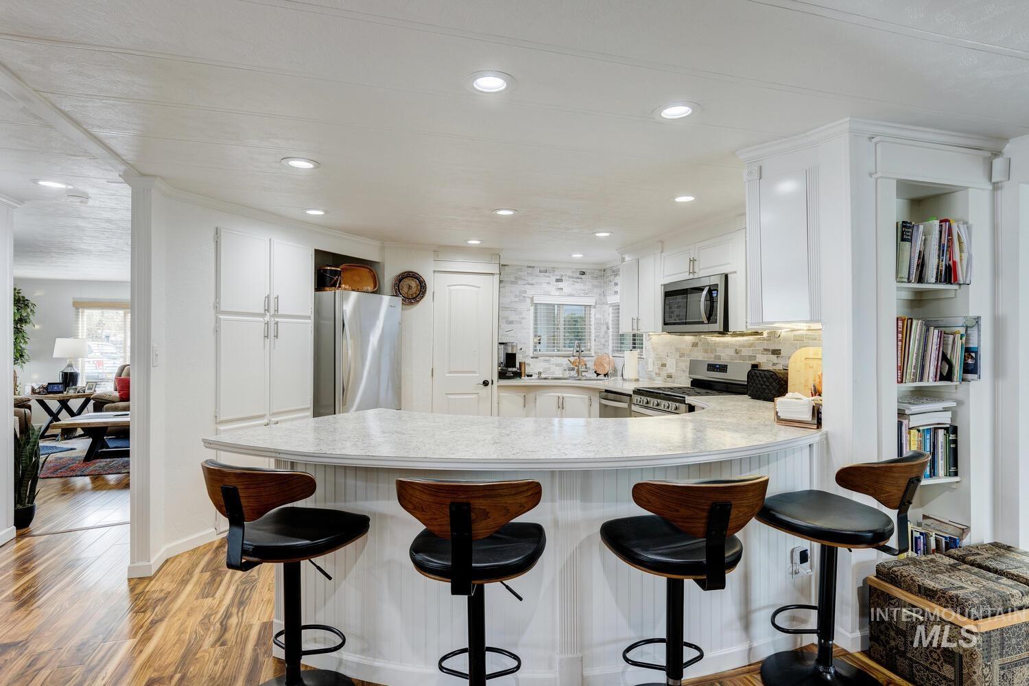 Kitchen with stainless steel appliances, tasteful backsplash, white cabinetry, a breakfast bar, and recessed lighting