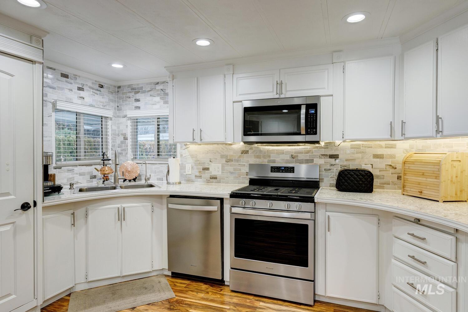 Kitchen featuring appliances with stainless steel finishes, white cabinets, recessed lighting, light wood-style flooring, and backsplash