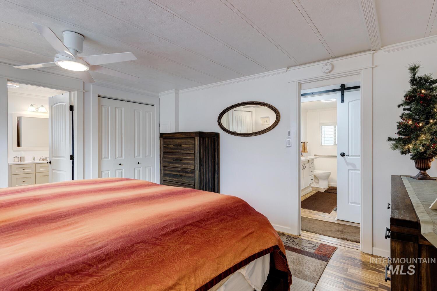 Bedroom with ensuite bathroom, a barn door, a closet, light wood-style flooring, and crown molding