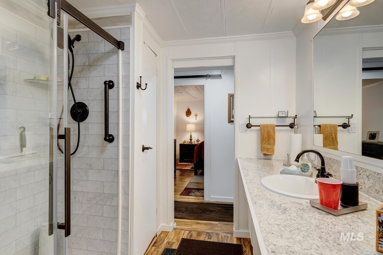 Ensuite bathroom featuring vanity, light wood finished floors, a stall shower, and ornamental molding