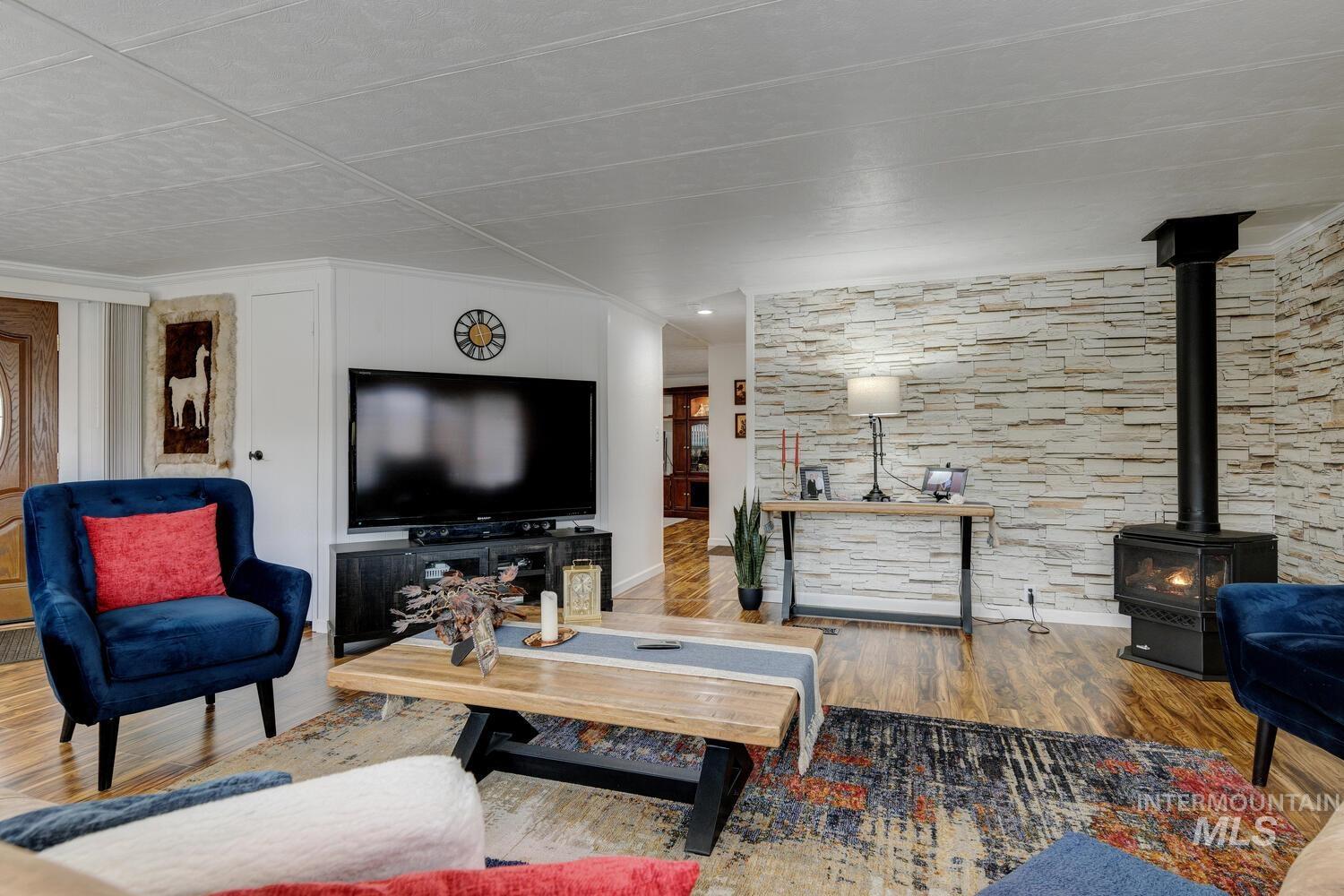 Living room with a wood stove, wood finished floors, and ornamental molding