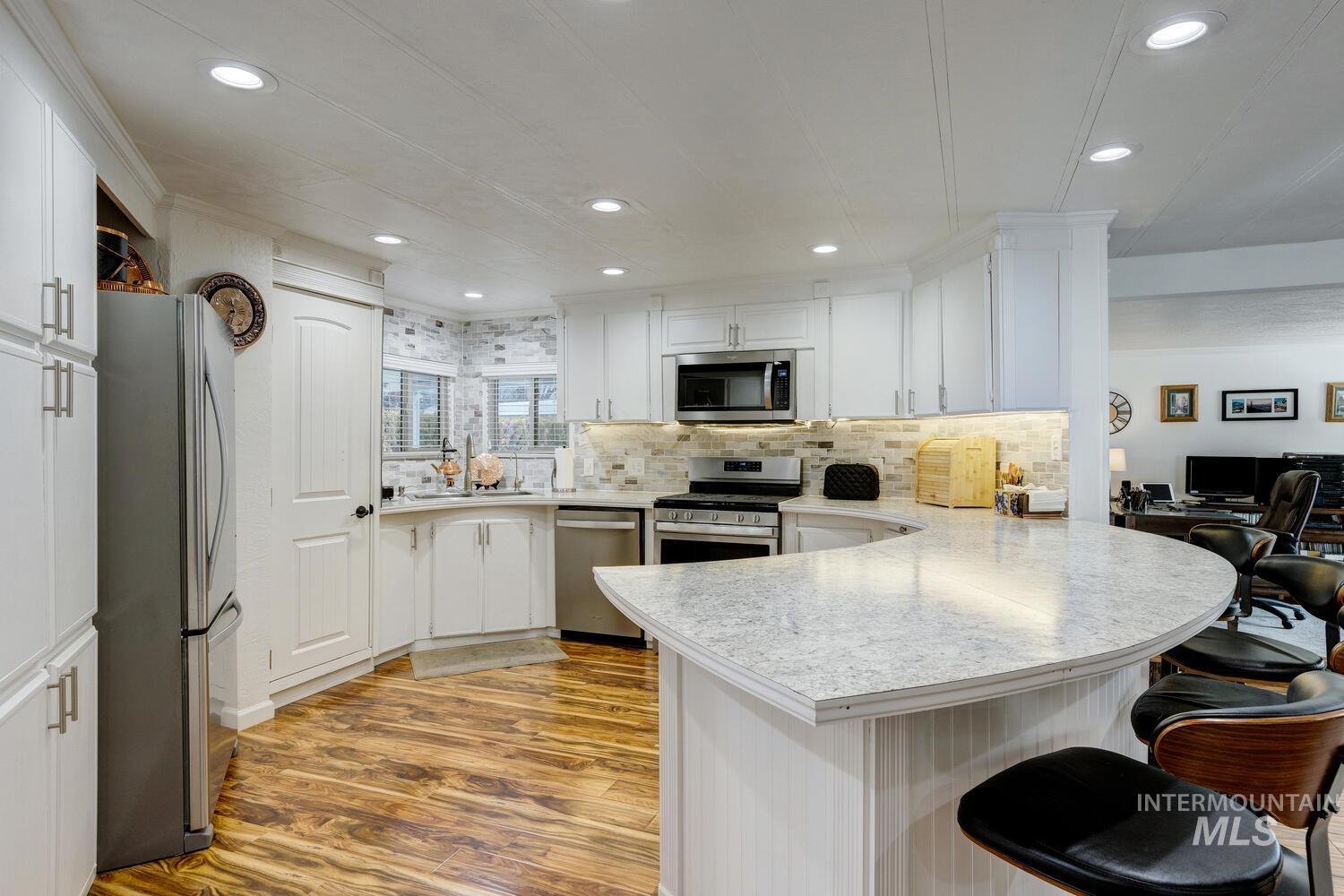 Kitchen featuring white cabinets, a kitchen bar, a peninsula, stainless steel appliances, and light wood finished floors