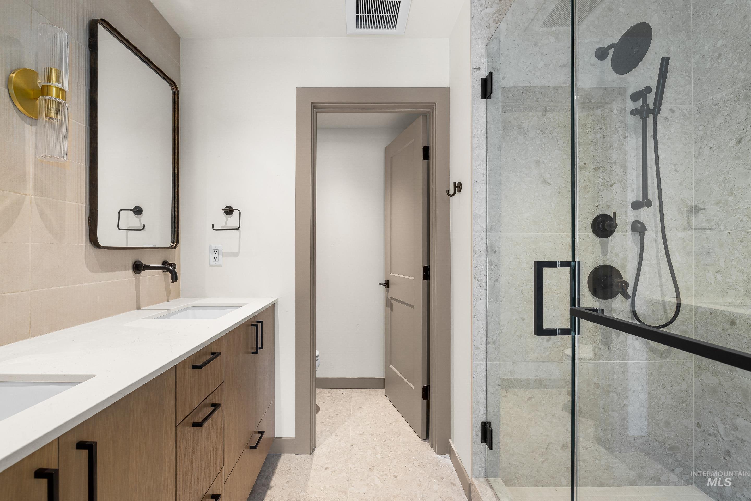 Bathroom featuring double vanity, a shower stall, and dark aggregate flooring