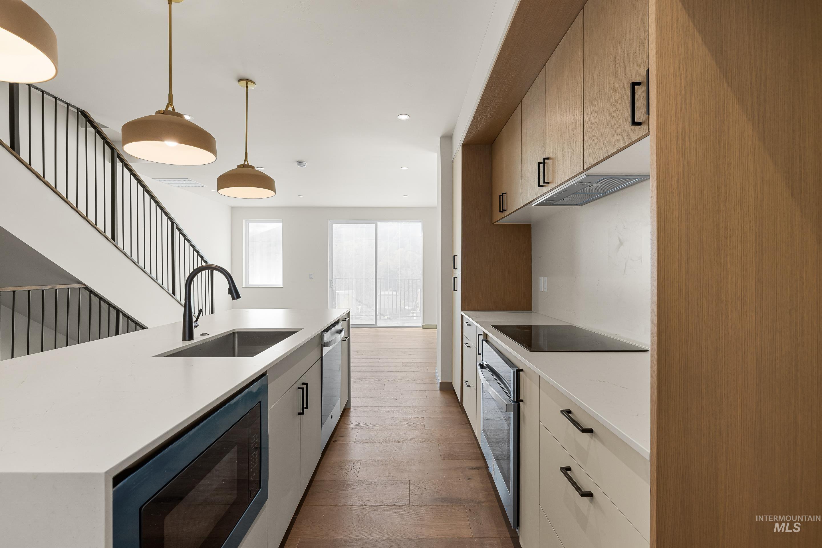 Kitchen with pendant lighting, black appliances, a center island with sink, light stone countertops, and hardwood / wood-style flooring