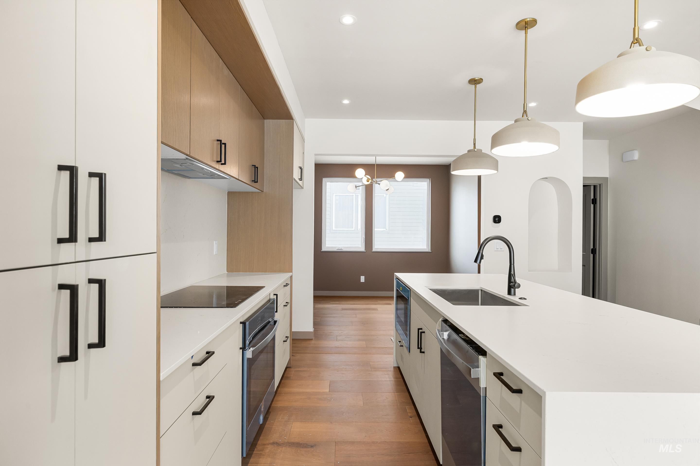 Kitchen with decorative light fixtures, light stone counters, a center island with sink, stainless steel appliances, and light wood-style flooring