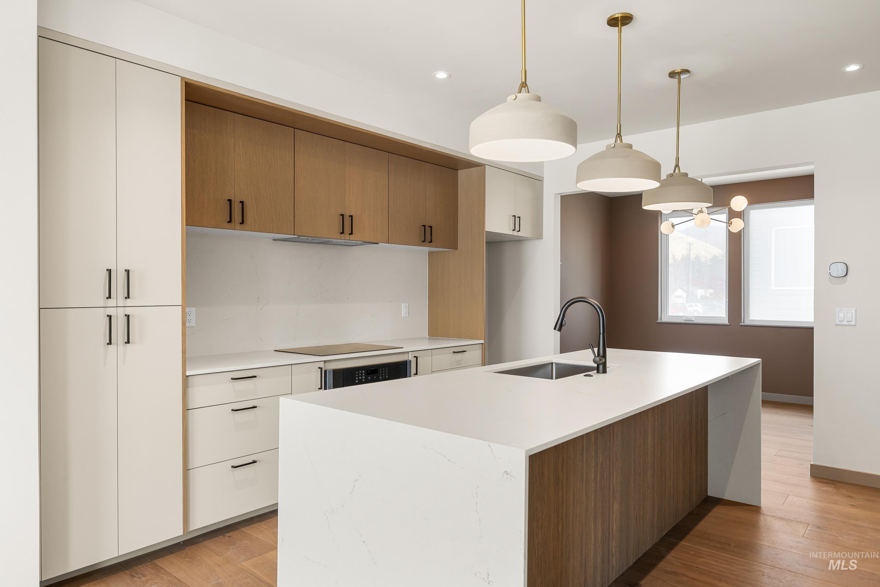 Kitchen with hanging light fixtures, a center island with sink, light stone countertops, light wood-style flooring, and recessed lighting