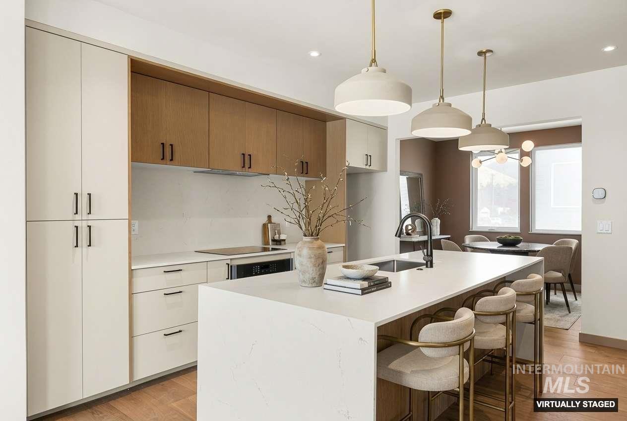 Kitchen featuring a kitchen island with sink, a breakfast bar area, hanging light fixtures, tasteful backsplash, and light wood-style flooring
