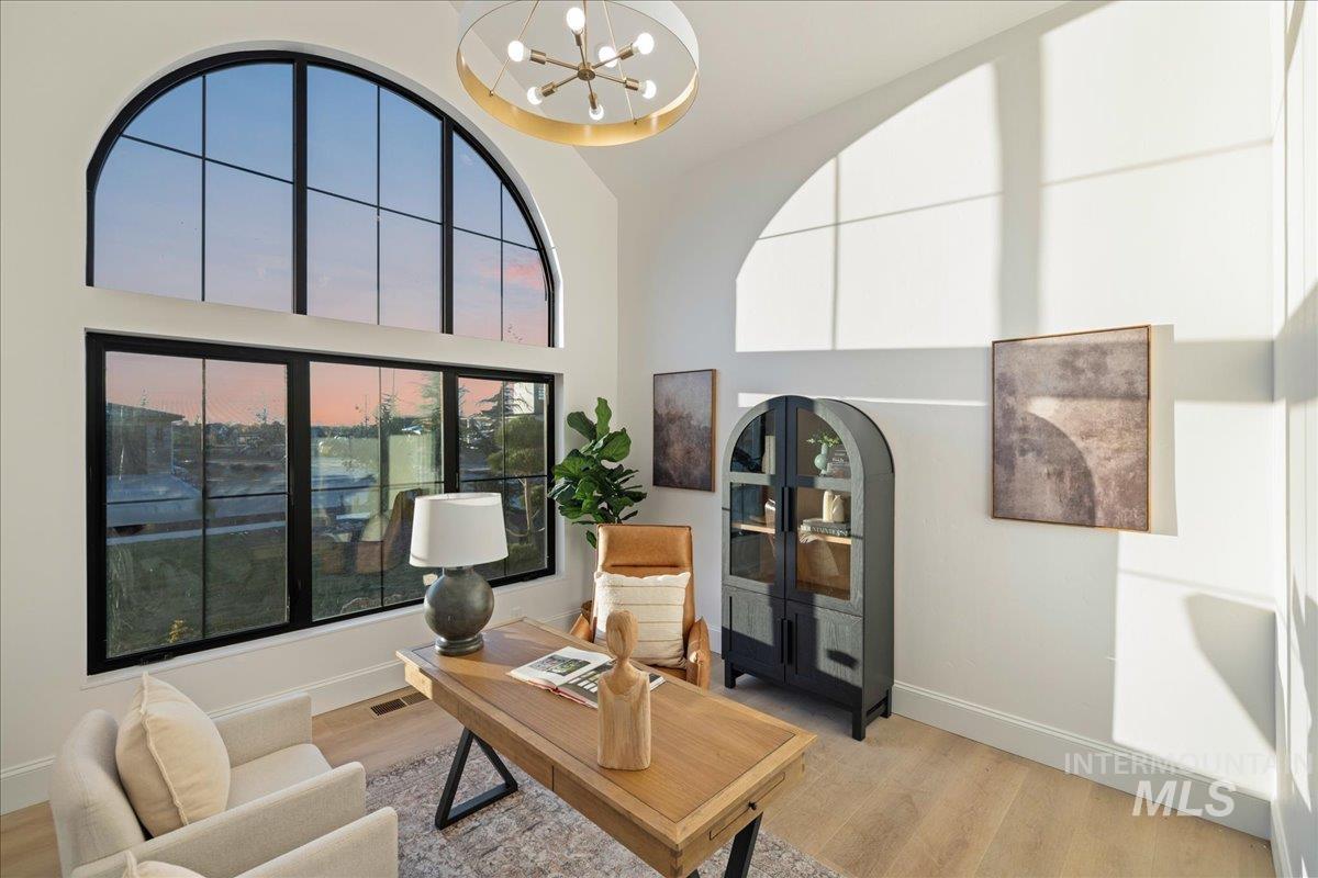 Living room with a chandelier, a desk, light wood finished floors, and a high ceiling