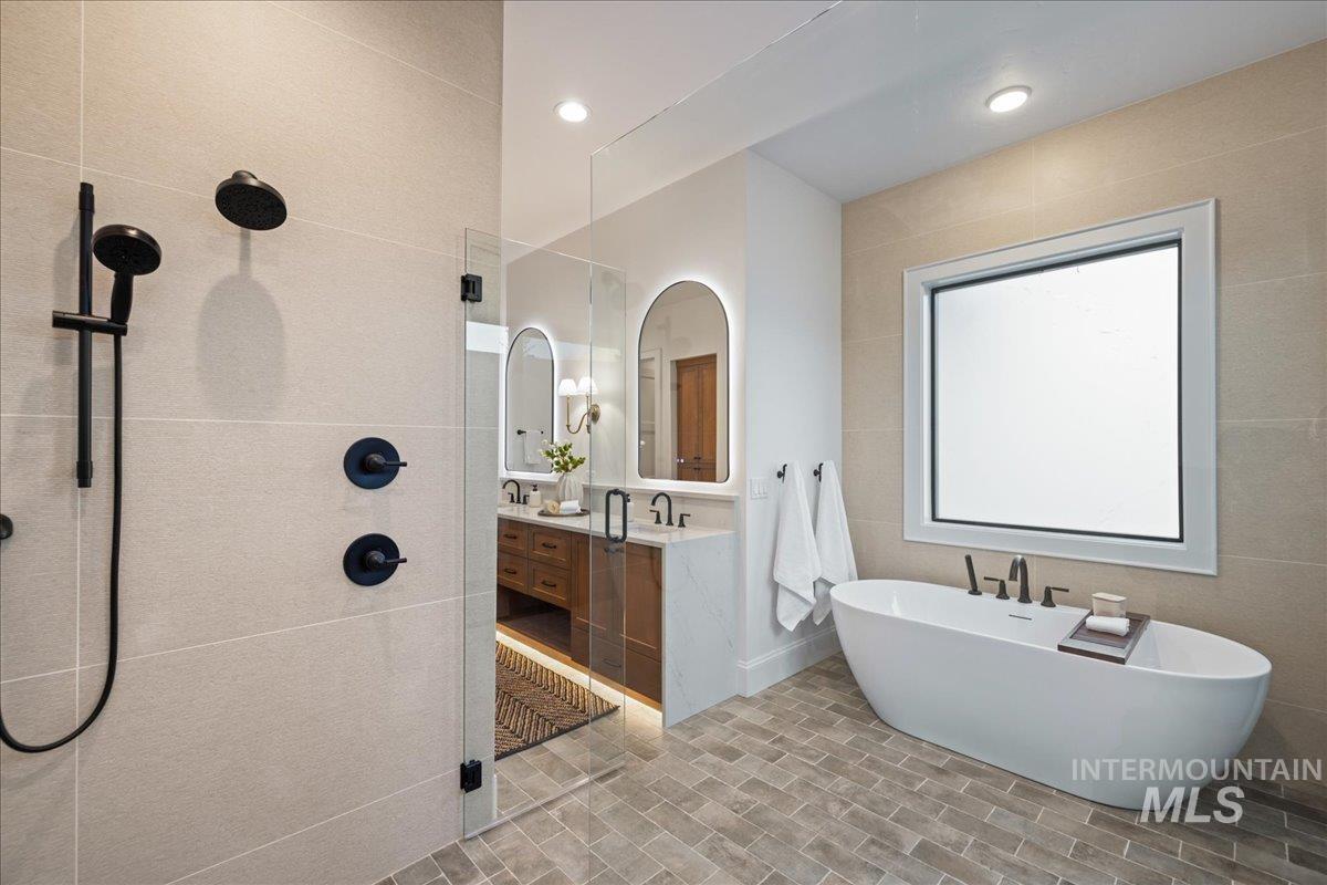 Bathroom with vanity, walk in shower, a soaking tub, and tile walls
