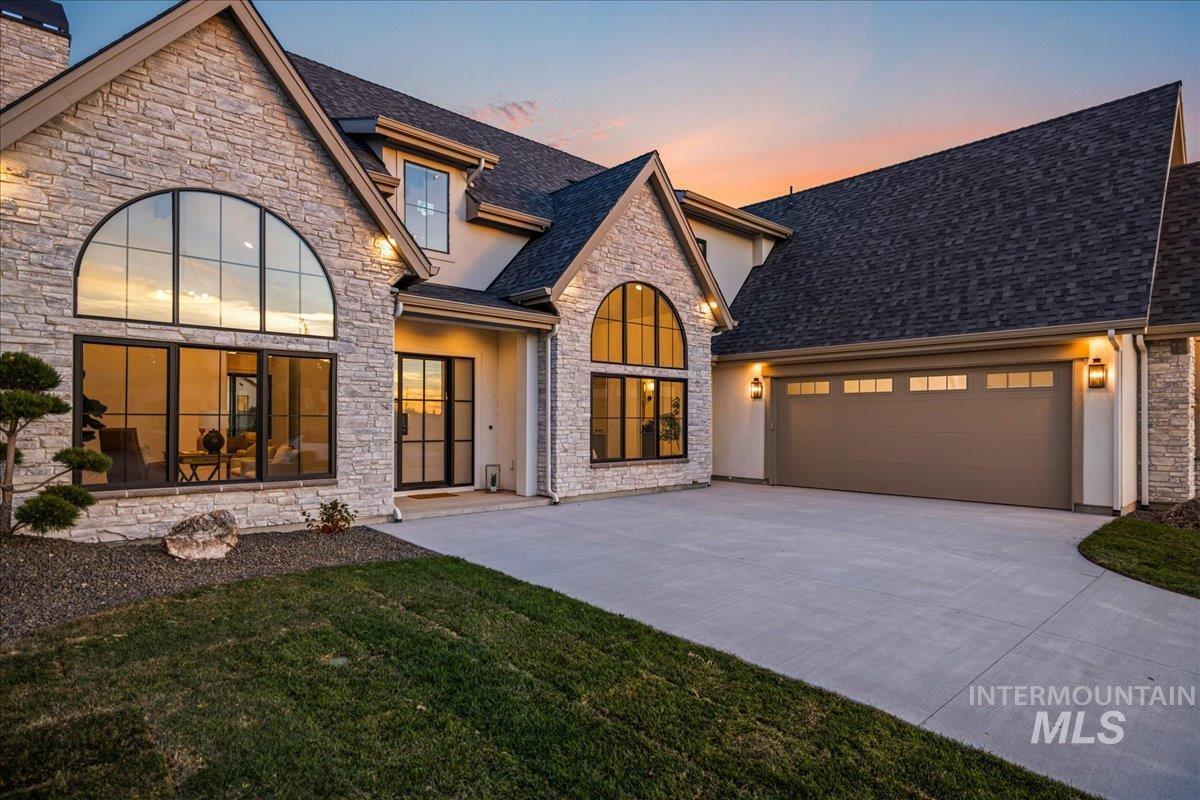 French country inspired facade with stone siding, stucco siding, an attached garage, and concrete driveway