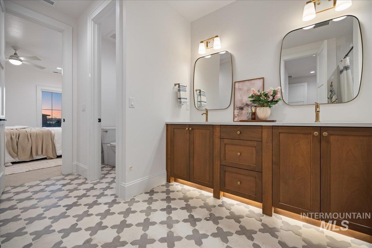 Ensuite bathroom featuring light flooring, double vanity, and a ceiling fan