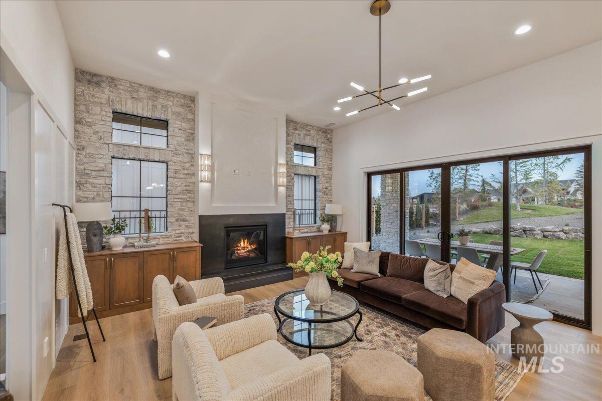 Living room with plenty of natural light, light wood-type flooring, a glass covered fireplace, a chandelier, and recessed lighting