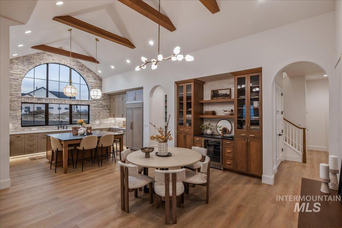 Dining area featuring high vaulted ceiling, beverage cooler, arched walkways, beam ceiling, and light wood finished floors