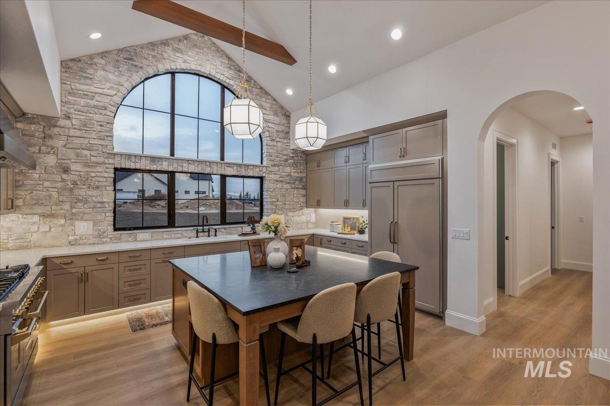 Kitchen with high end appliances, high vaulted ceiling, gray cabinets, arched walkways, and hanging light fixtures