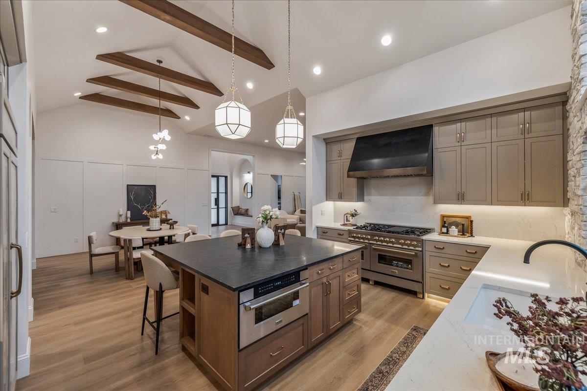 Kitchen featuring gray cabinetry, a center island, high quality appliances, premium range hood, and a kitchen bar