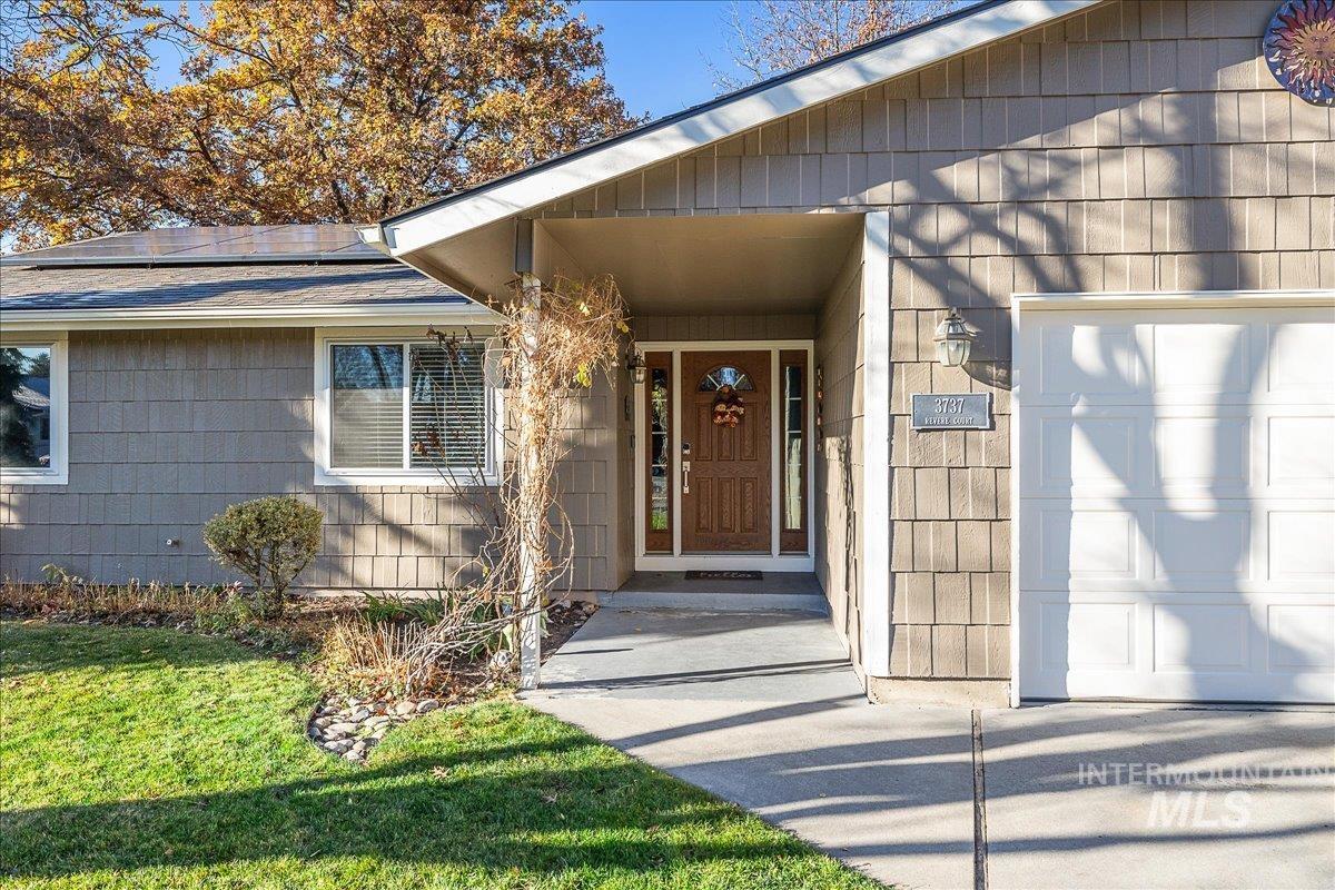 Doorway to property with a garage, a shingled roof, a lawn, and solar panels
