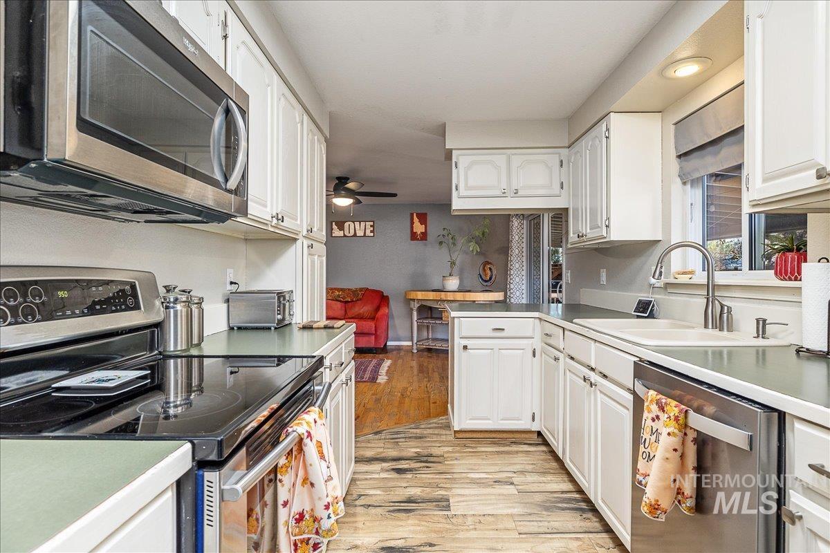 Kitchen featuring appliances with stainless steel finishes, light wood-style floors, a peninsula, white cabinets, and a ceiling fan