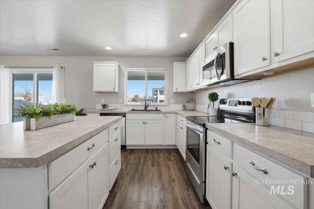 Kitchen featuring stainless steel appliances, white cabinetry, a textured ceiling, dark wood finished floors, and light countertops