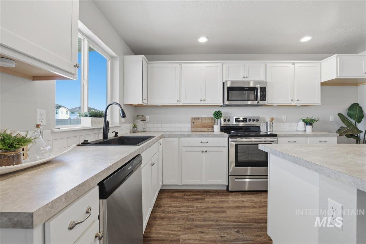 Kitchen with white cabinetry, stainless steel appliances, dark wood finished floors, light countertops, and recessed lighting