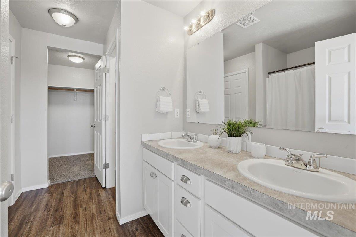 Bathroom featuring a walk in closet, double vanity, curtained shower, and dark wood-style floors