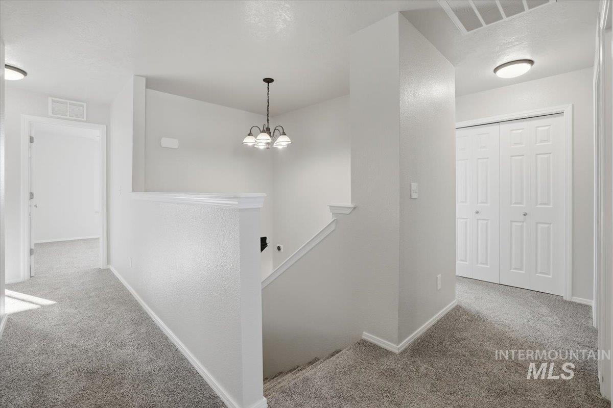 Hallway with an upstairs landing, carpet floors, and a chandelier