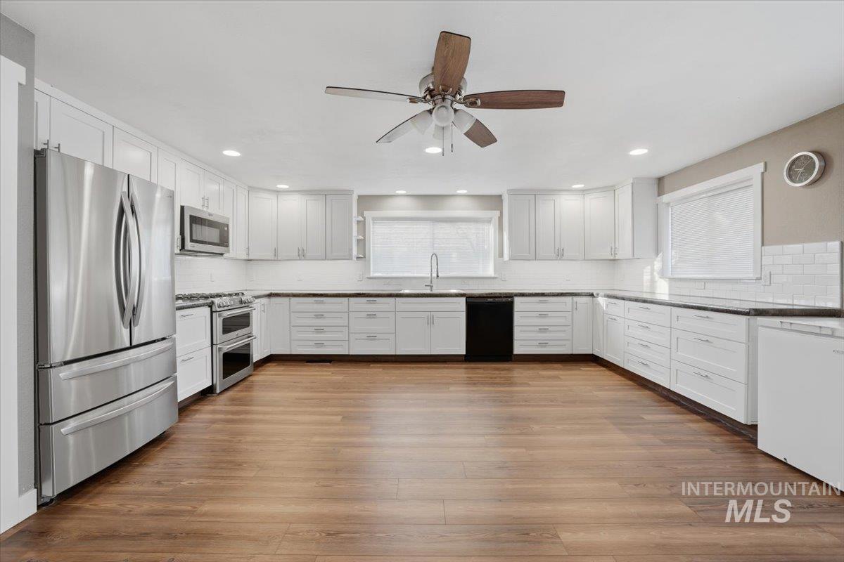 Kitchen with stainless steel appliances, white cabinets, and dark wood-style floors