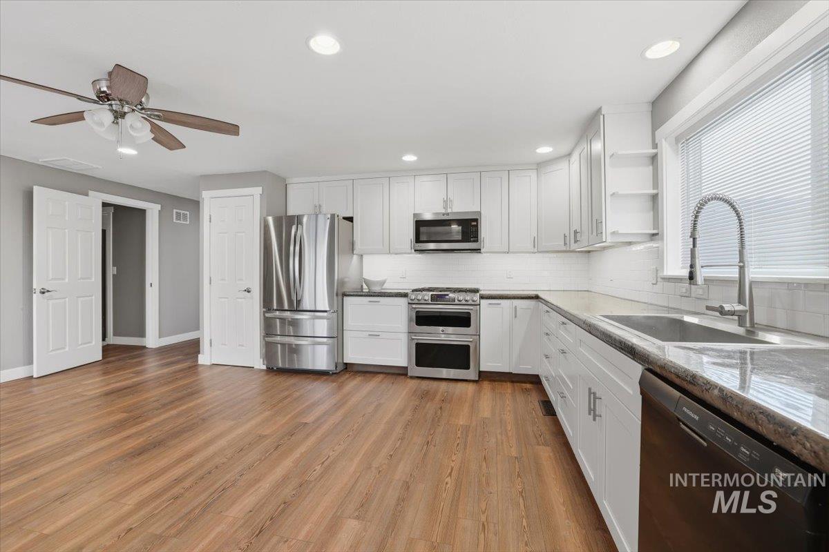 Kitchen featuring appliances with stainless steel finishes, white cabinets, open shelves, light wood-style floors, and recessed lighting