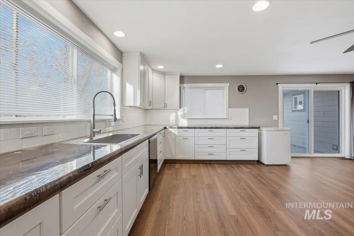 Kitchen featuring white cabinets, light wood-style flooring, dark stone countertops, white fridge, and tasteful backsplash