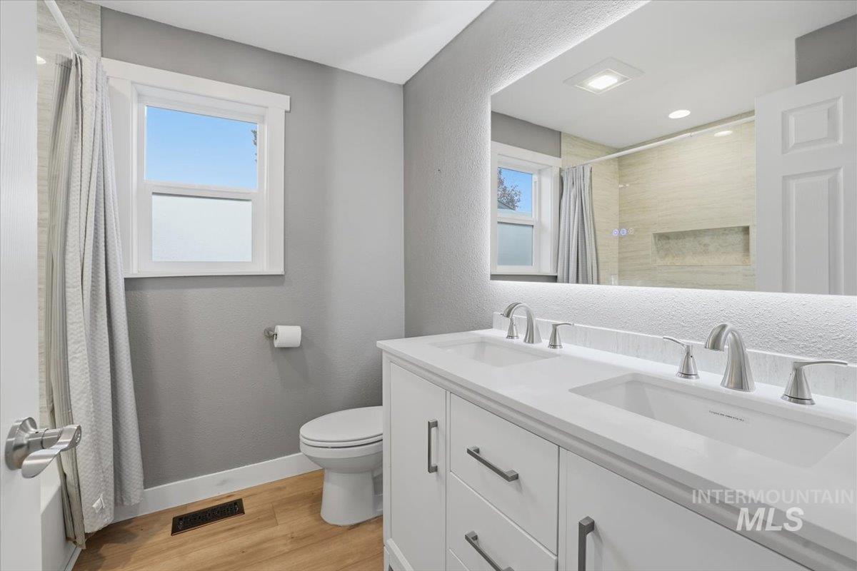 Bathroom with a textured wall, light wood-style floors, double vanity, and a shower with curtain