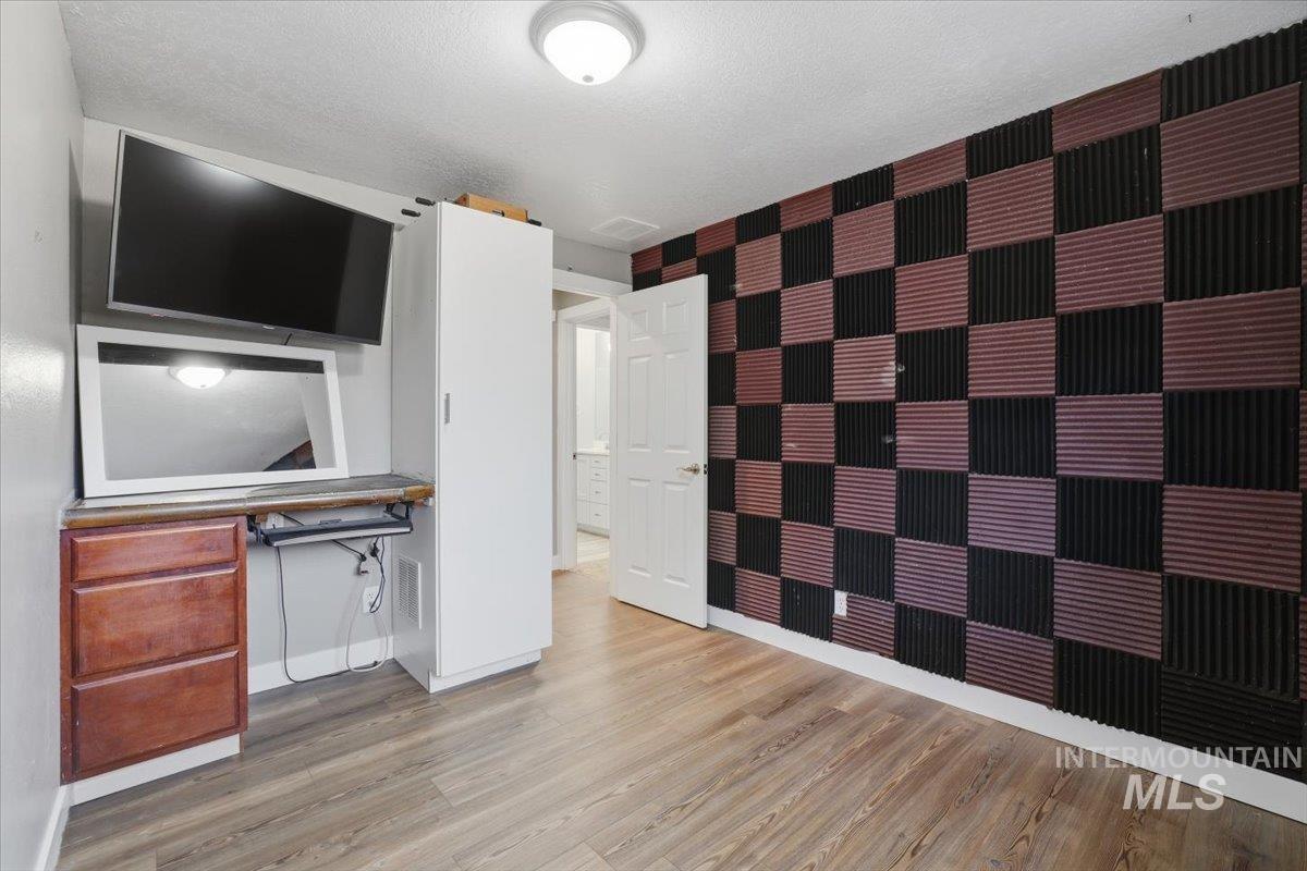 Interior space with an accent wall, light wood-style flooring, a textured ceiling, wallpapered walls, and a desk