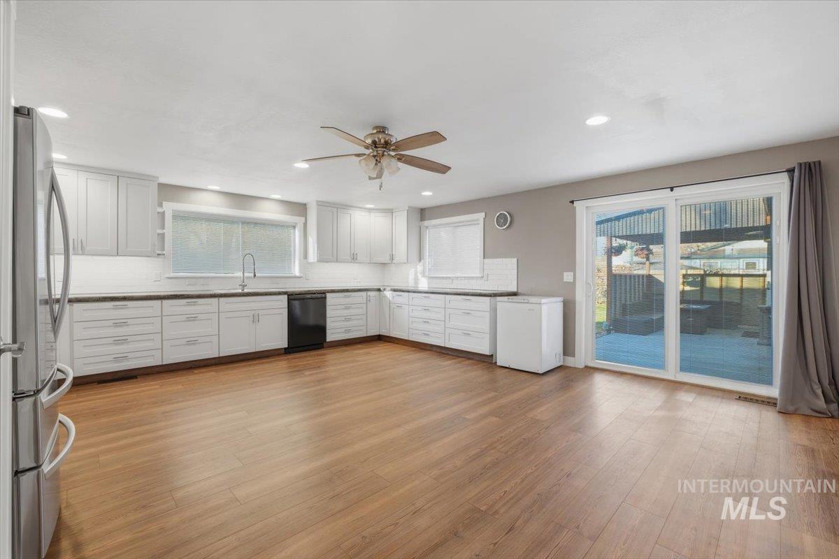 Kitchen with white cabinets, tasteful backsplash, freestanding refrigerator, light wood finished floors, and black dishwasher